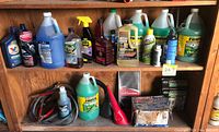 Wide shot showing multiple automotive fluid containers, jumper cables, and other car supplies arranged on wooden shelves.