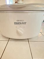 Close-up photo of the Rival Crock-Pot slow cooker showing brand name, control dial with Off, Low, High settings, white exterior with stoneware finish.