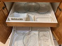 Wide view of two cabinet drawers showing various glass bakeware including clear pie plates and white Corningware dish with floral design