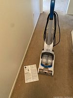 Front view of the Hoover Powerdash steam cleaner on a carpet with owner's manual placed beside it.