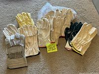 Image showing approximately 15 pairs of work gloves with various colors and cuff styles, mostly leather, some still in original packaging.