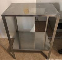 Front view of the metal workspace table showing the top flat surface and the lower shelf with the four supporting legs.