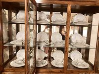 Twelve complete place settings displayed on glass shelves in wooden cabinet