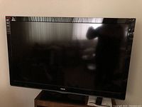 Front view of RCA 46 inch LCD TV mounted on a stand, screen off showing black glossy display and RCA logo on bottom bezel.