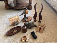 Full view of the entire collection of wooden knickknacks on carpeted floor showing diverse items including carved birds, wooden tray, toy car, hands, and business card holder