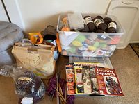 Overview of yarn skeins, knitting needles, craft books, and storage bags arranged near wall.