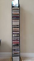 Full view of black metal CD storage tower filled with approximately 90 assorted music CDs.