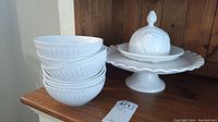 Six white porcelain bowls stacked, covered dish on pedestal serving tray in background