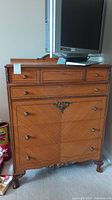 Front view of vintage wood and veneer dresser showing all seven drawers, pulls, and floral filigree accents