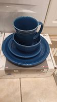 Three-piece blue Fiestaware dinnerware set stacked on the box: plate, bowl, mug.
