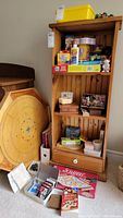 Full view of board games including Crokinole board, Snakes and Ladders, Scrabble box, and other games arranged on shelf and floor.