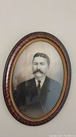 Front view of oval portrait in a wood veneer frame with convex glass showing full portrait and frame details.