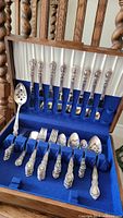 Full view of flatware set in blue velvet lined wooden canteen with dinner forks, spoons, teaspoons, salad forks, and serving spoon.