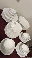 Overview of all stacked plates, cups, saucers, and bowls on table