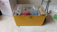 Full closed view of yellow sewing box with clear lid on carpeted floor