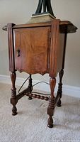 Front and side view of vintage wood smoking table showing scalloped edges, cabinet door with keyhole, turned legs, stretcher bar, and top surface with lamp base.