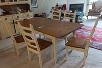 Full view of rectangular dining table with six matching ladder back chairs arranged on carpet in a room with a hutch in the background.