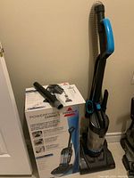 Full photo showing the Bissell vacuum upright with hose and crevice attachment on top of the box.