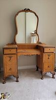 Front view of vintage mahogany vanity with large curved mirror and carved floral accents.