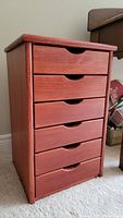 Front view of wood cabinet showing six drawers with flush cut out pulls and reddish finish.