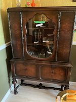 Front view of wooden china cabinet showing glass display door with lock and two lower paneled doors on carved legs.