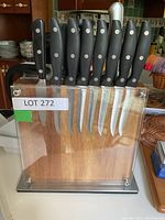Front view of the knife set with nine knives in magnetized wooden block with clear acrylic sides and metal base.