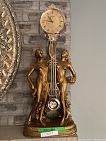 Front view of decorative clock showing two bronze-gold female figures holding an ornate clock and pendulum