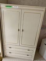 Full view of white vintage dresser showing two doors on upper portion and two drawers at bottom with gold trim detail.