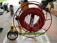 Electric cord wound tightly on a red metal reel with a yellow flashlight attached.