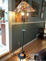 Full view of the floor lamp showing stained glass style floral shade, slim pole, and black metal base with curled feet.