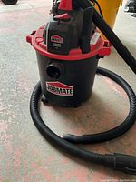 Front angled view of Jobmate 4-gallon shop vac with attached hose on a concrete floor.