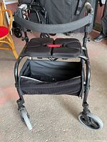 Front view of black Nexus rollator walker showing split padded seat, three wheels, and storage basket beneath seat.