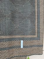 Close-up image showing the woven texture and black and brown geometric patterned border of the carpet.