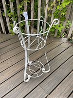 Front angle view of the white metal garden planter stand showing its shape, legs, and scroll ends.