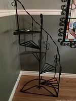Full view of black metal spiral staircase style plant stand against wall.