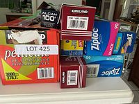 Photo showing several boxes of plastic wrap, parchment paper, aluminum foil, and Ziploc bags stacked on a kitchen counter, with a lot number sticker visible.