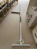 Full view of the white adjustable assistive pole laid out on beige carpet next to a brass bedframe and floral painted box.