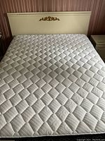 Photo showing queen bed mattress on bed frame with cream-colored headboard with gold floral decoration.