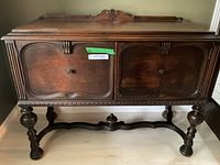 Front view of the antique wooden sideboard showing the carved cabinet doors, knobs, and ornate leg design.