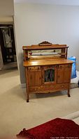 Front view of antique oak sideboard with top mirror and carved wood detailing.