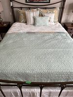 View of bed made with two quilted comforters and all five pillows arranged on a metal frame bed, showing color and texture of linens.