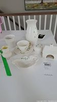 Full set of Belleek china items on table showing vase, cup and saucer, jewelry box, candle holder, creamer, and decorative dish