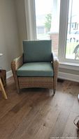 Front view of wicker chair with cushions, showing woven wicker, padded cushions in light teal, and chair proportions.