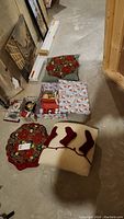 Top view photo of 8 poinsettia and pinecone placemats, knitted pillow with stockings, gift boxes and wrapping supplies arranged on floor.