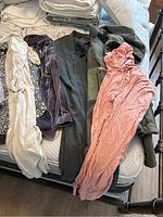 Photo showing assorted women's clothing items laid out on a mattress including cardigans, dresses, and tops in colors cream, gray, purple, and pink.