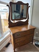 Full view of wooden dresser with attached mirror showing front and side, highlighting the wood grain and carved decorative details on mirror frame and dresser.