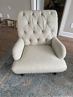 Front view of cream-colored upholstered armchair with vertical stripes and button tufting on backrest.