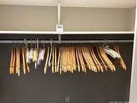 Wide view of multiple wooden hangers with some padded and plastic hangers mixed in on metal hanging rod.