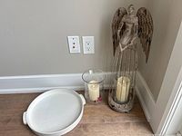 Wide view showing white ceramic tray, two electric candles in glass holders, and metal angel decoration.