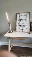 Desk lamp next to wooden wall hanging sign visible on white desk